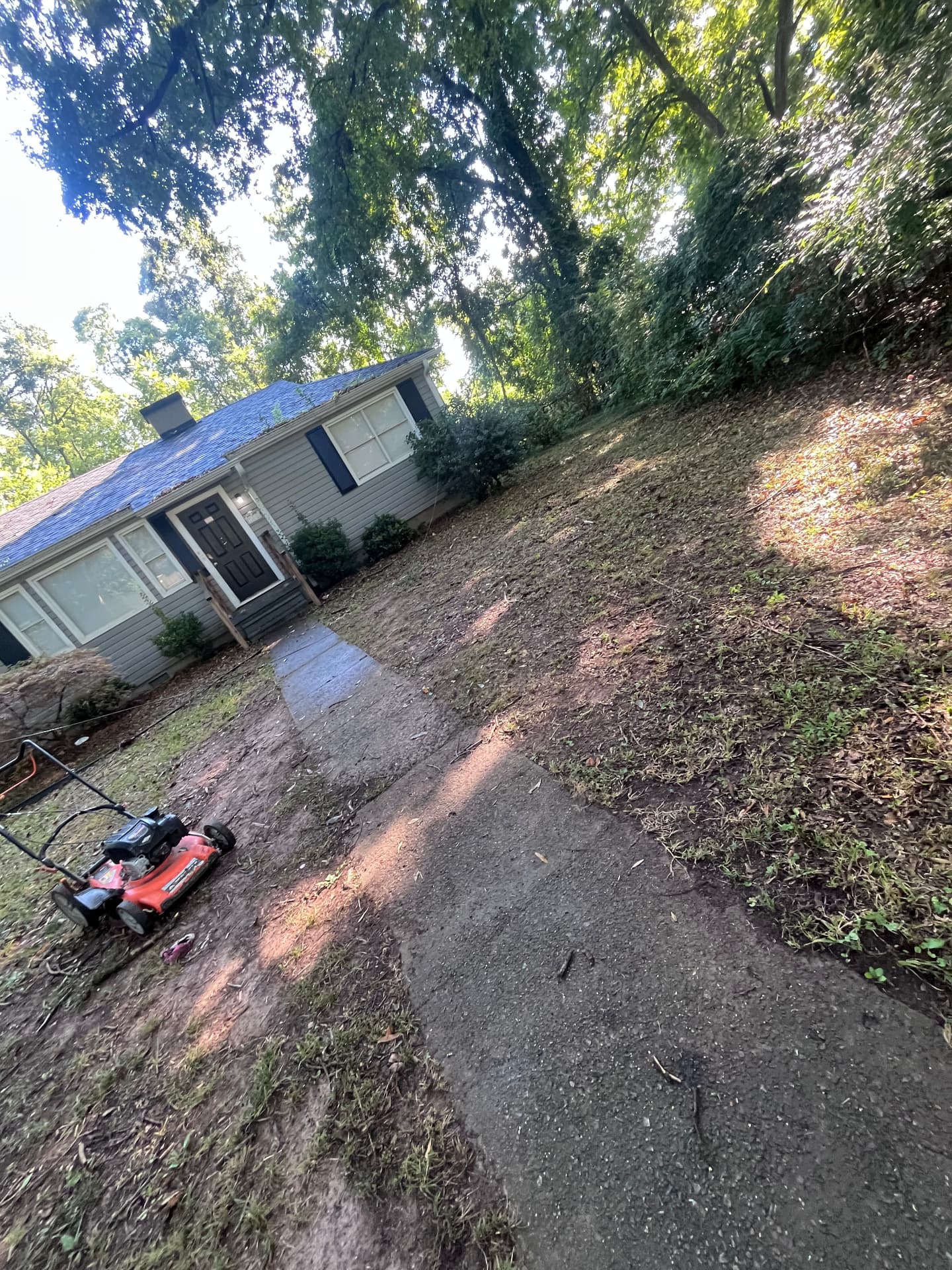 Gray house with a concrete walkway and a red push mower, yard mid-cleanup.