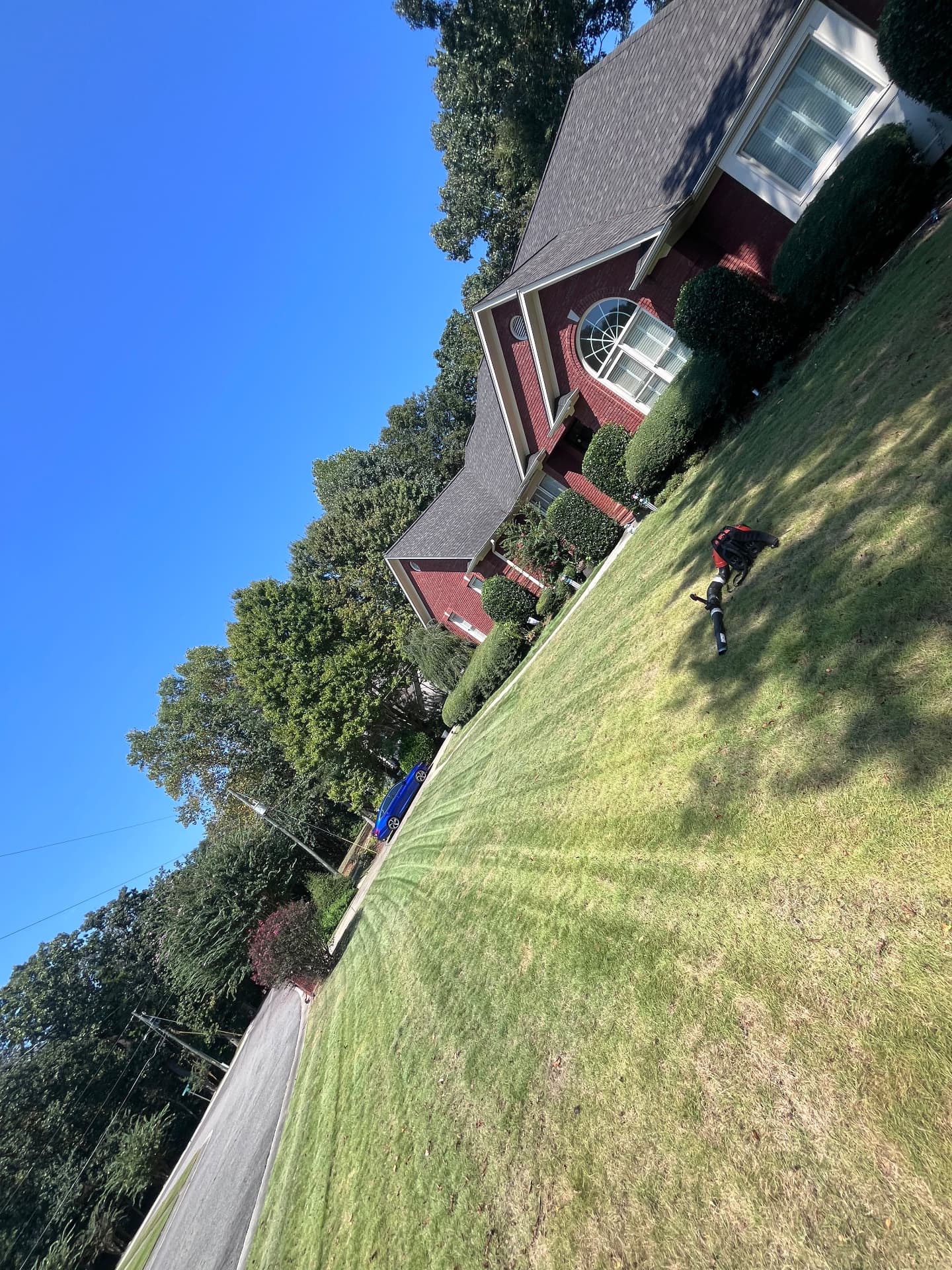 Two-story red brick home with a wide green lawn showing fresh mowing stripes and a leaf blower on the grass.